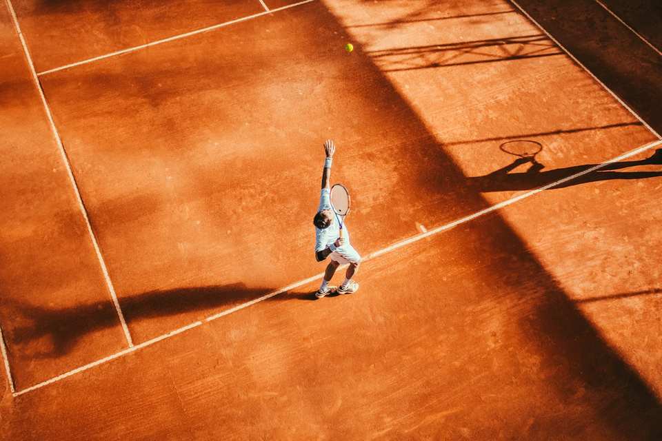 Tennis player practising a serve on a clay court